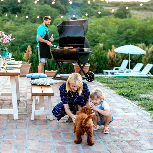 Mamá e hija juegan con el perro mientras el papá prepara la barbacoa