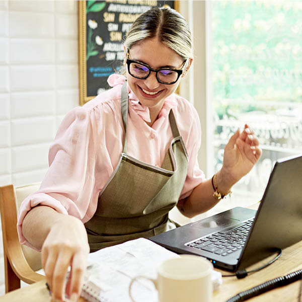 Woman business owner in glasses using laptop and smiling