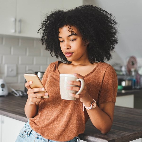 Mujer de pelo rizado con una taza de café y mirando su celular