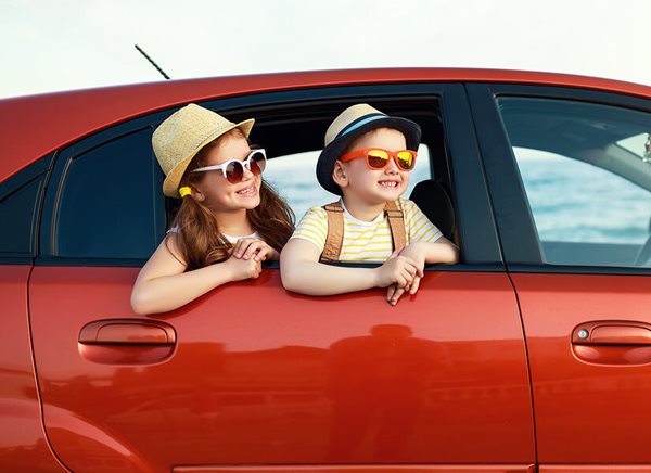 Dos niños en la parte de atrás de un auto rojo.