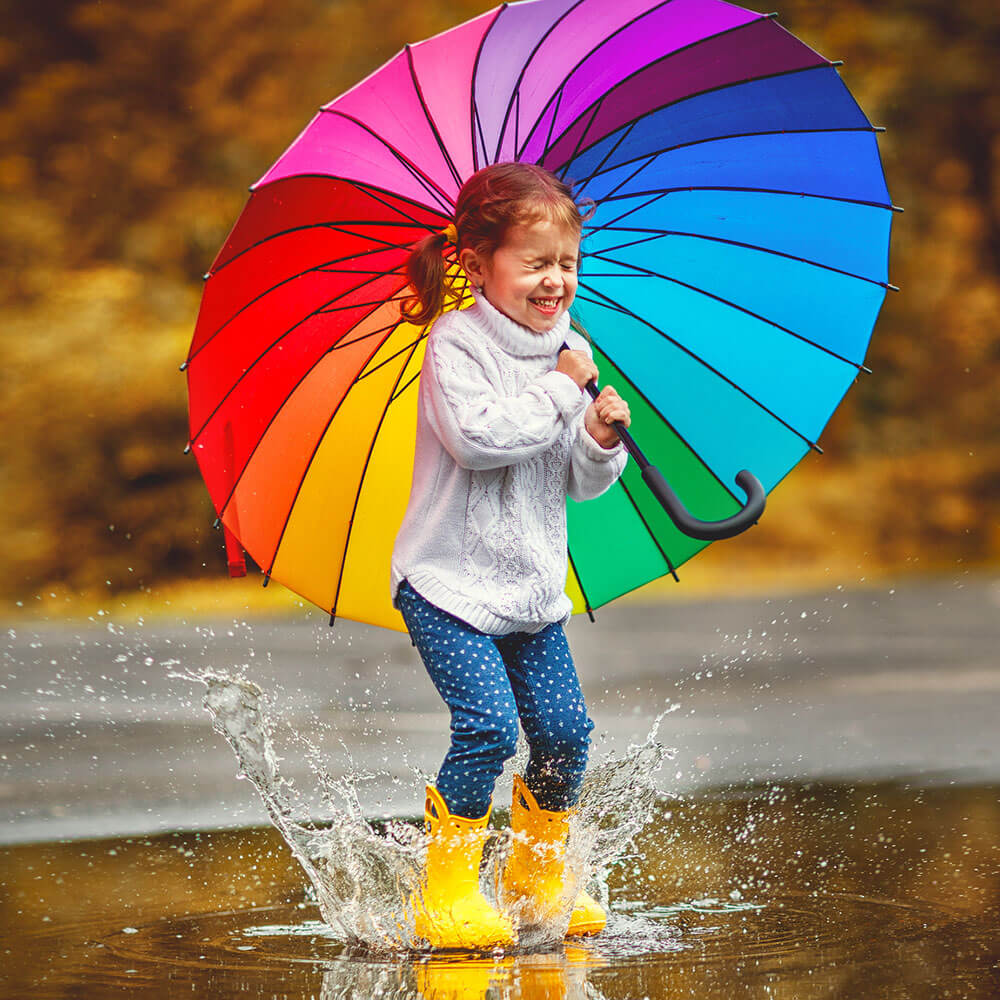 Niña con paraguas multicolor saltando en un charco